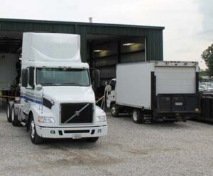 A white semi and box truck parked in front of a warehouse