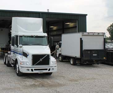 A white semi and box truck parked in front of a warehouse