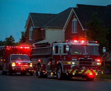 Two fire trucks with lights on in front of a house