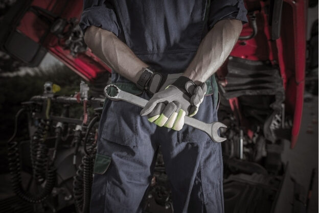 A closeup of a technician holding a wrench and wearing gloves.